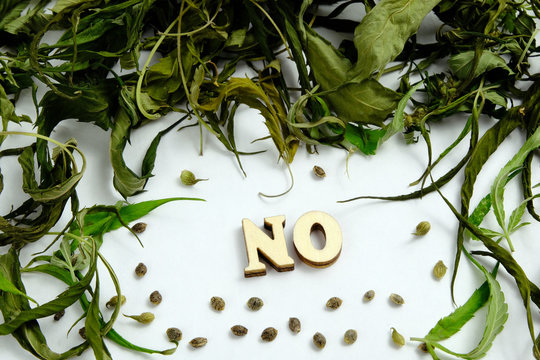 The word NO is laid out of wooden letters. The frame is composed of dry leaves of marijuana and cannabis grains.