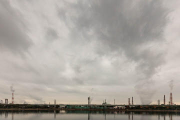 Fototapeta na wymiar Emissions from factory mix with clouds over water