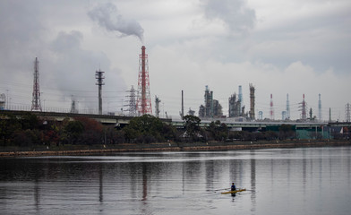 Obraz premium Single rower in front of large industrial complex with smokestacks