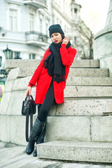 Portrait of a young beautiful fashionable woman in a red coat . Model posing on a city street