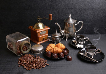 Coffee still life. A cup of coffee, a coffee pot, a coffee grinder and sweets on the table