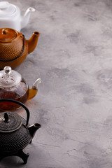 A variety of teapots in a row on a gray textured background. The concept of tea drinking.