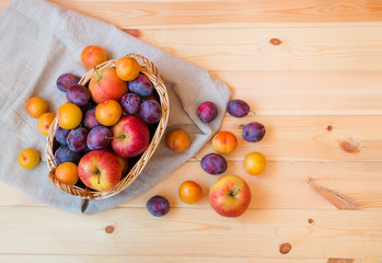 Wicker basket with apples and colorful plums on wooden table. Top view.
