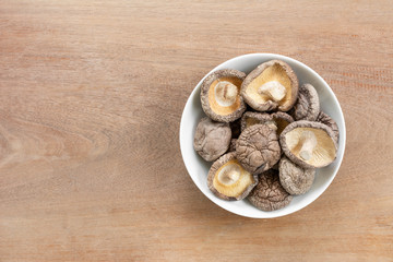 top view of dried shiitake mushroom in a ceramic dish on wooden table with copy space for text. healthy food and medical concept.