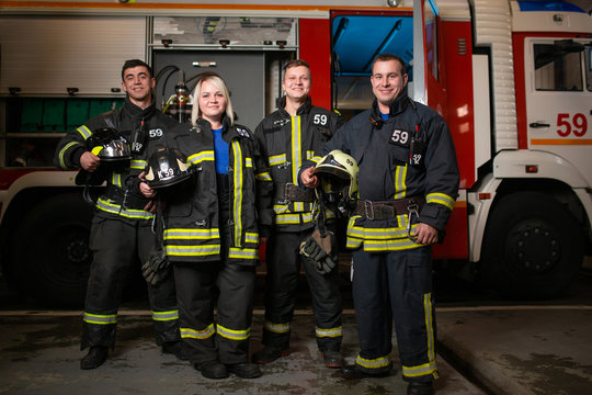Full-length image of three young fire men and woman on background of fire truck