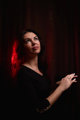 Mysterious portrait of a girl in a black dress in dark room and red light background