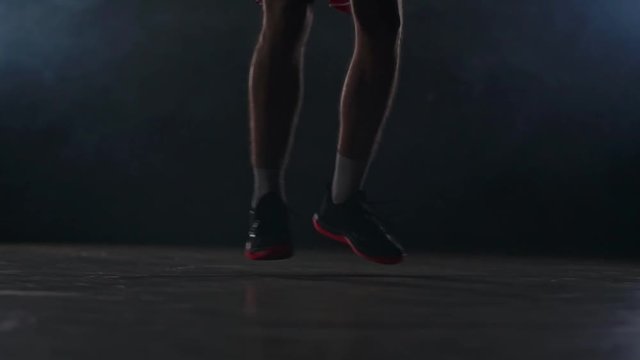 Male athlete in sportswear and sneakers prokipyvaet basketball ball between legs on the basketball court in the smoke in slow motion