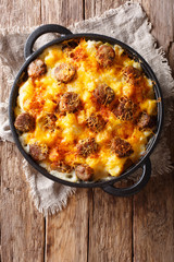 Delicious potato casserole, sausages with cheese sauce close-up in a frying pan. Vertical top view