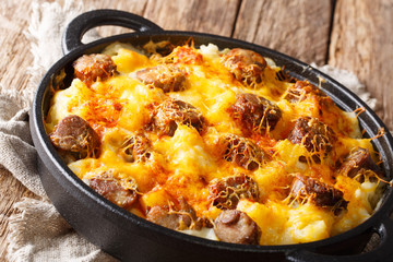 Traditional casserole of potatoes, smoked sausages with cheese sauce close-up in a frying pan. horizontal