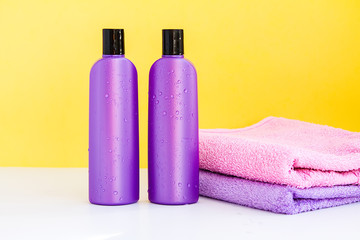 two purple cosmetic bottles and two towels on a lilac background