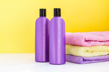 two purple cosmetic bottles and three towels on a lilac background