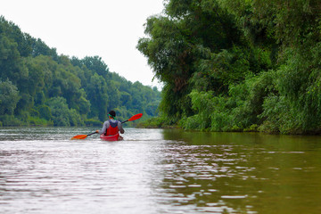 Rear view of teenager paddle red kayak on summer Danube river. Summer kayaking. Concept for adventure, travel, action, lifestyle