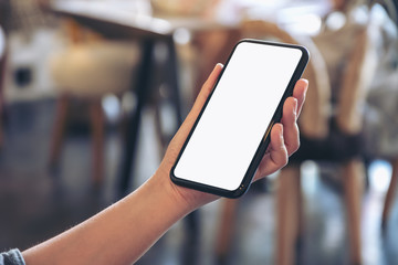 Mockup image of a hand holding black mobile phone with blank white desktop screen in cafe