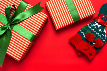 Fototapeta premium Woolen socks with a Christmas New Year ornament and gift box on red background top view flat lay. Holiday concept, presents Xmas. Congratulations background with space for text.