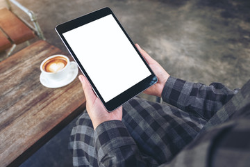 Mockup image of woman's hands holding black tablet pc with blank screen with coffee cup on wooden table in cafe