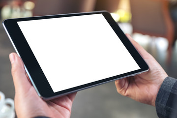 Mockup image of hands holding and using black tablet pc with blank white desktop screen in cafe