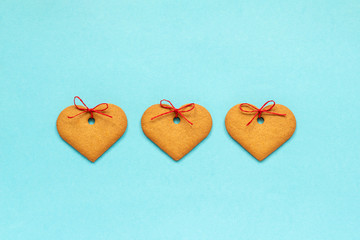 Ginger cookies heart-shaped decorated with a bow arranged in a row on a blue background. Top view Copy space Valentine card.