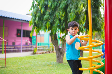 Obraz premium Active Asian Kid playing climbing metal spiral at school yard playground. Kids play and climb outdoors.