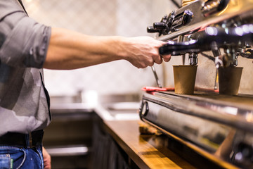 Barista grinding coffee beans using coffee machine, coffee grinder grinding freshly roasted make beans into a powder.