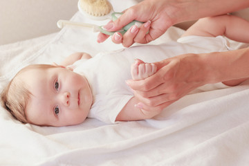 Baby and hands of mother with a baby hair brush, indoors, blurred background