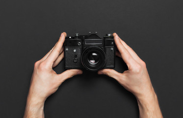 Male hands hold old vintage camera on black background top view flat lay with copy space. Concept for the photographer, old photographic equipment, minimalistic style