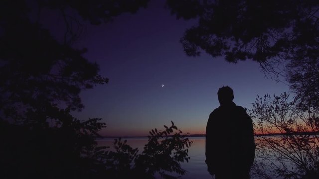 Dark night lonely man with a lamp stands on the banks of the river