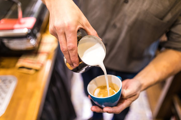 Close up of male hands pouring milk and preparing fresh cappuccino. Coffee artist and preparation concept. Morning coffee
