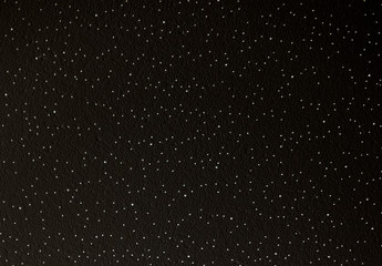 Stars randomly located. White holes pierce through the material. Black texture of stone or metal. Christmas