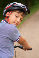 Back view of cheerful little guy in protective sportswear riding a bike