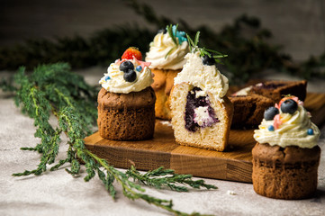 Close up. Freshly baked blueberry-lavender muffins, one of them in the cut. Top decorated with a cream hat with berries. Gray background.