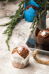 Close up. Fresh baked chocolate muffins. Top decorated with a cream hat with Christmas snowflakes of mastic. Gray background. Green branches of a fragrant juniper.