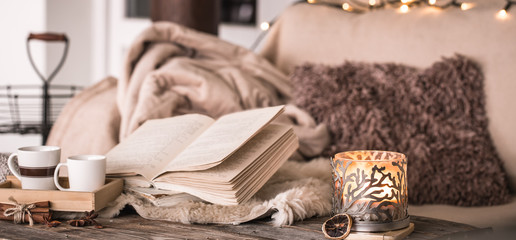 still life home atmosphere in the interior with cups, a book and candles, on the background of cozy bedspreads