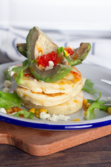 pancakes with avocado and caviar on a white plate.