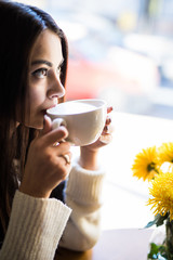 Close up portrait of young beautiful happy woman drinking coffee and looking through the window.