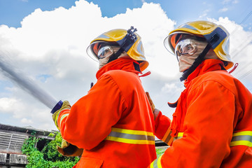 Fototapeta premium Two fireman trainning in fire fighting suit spraying water to fire surround on house background