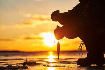 The angler fisherman at ice winter fishing. Sunset