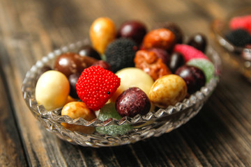 Different candies in a crystal bowl on old wooden table. Multi colored gummy candy coated with sugar, chocolate and fruit candy.