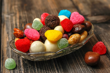 Different candies in a crystal bowl on old wooden table. Multi colored gummy candy coated with sugar, chocolate and fruit candy.