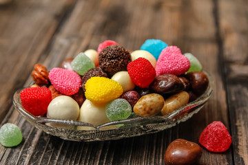 Different candies in a crystal bowl on old wooden table. Multi colored gummy candy coated with sugar, chocolate and fruit candy.