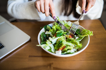 Close up attractive woman hand holding fork and spoon to eating vegetable salad at lunch in cafe. Healthy and vegetarian food.