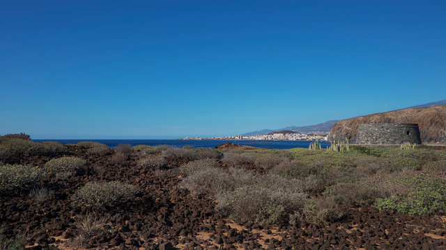 Arid volcanic landscape of Malpais de la Rasca, a natural reserve close to Palm-Mar town, with views towards Atlantic Ocean and the tourist resort Los Cristianos, in Tenerife, Canary Islands, Spain 