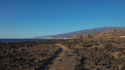 Path through the landscape of Malpais de la Rasca, a natural reserve close to Palm-Mar town, with views towards Atlantic Ocean and the tourist resort Los Cristianos, Tenerife, Canary Islands, Spain 