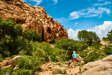 A tourist woman looking at red sand rocks in Calanques de Piana Corsica on sunny day