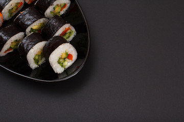 Sushi rolls in nori seaweed sheets on plate with black background.