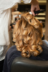 Hairdresser making styling with beautiful curls while girl sits in chair. Fabulous volume blonde hair in beauty salon.