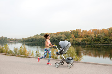 Active mother jogging. Jogging or power walking woman with pram at sunset. Mother with child in...