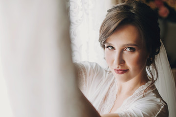 Beautiful stylish brunette bride posing in silk robe near wedding gown in the morning. Sensual portrait of happy woman model  getting ready for wedding day