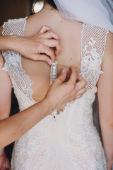 Bridesmaids helping bride get dressed in the morning. Hands on buttons on  amazing gown of gorgeous bride back. Beautiful woman getting ready in the morning. Wedding preparations