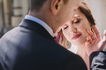 Gorgeous bride and stylish groom gently hugging and embracing in sunny street. Portraits of beautiful happy wedding couple. Romantic sensual moment touch. True love