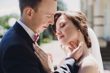 Gorgeous bride and stylish groom gently hugging and embracing in sunny street. Portraits of beautiful happy wedding couple. Romantic sensual moment touch. True love
